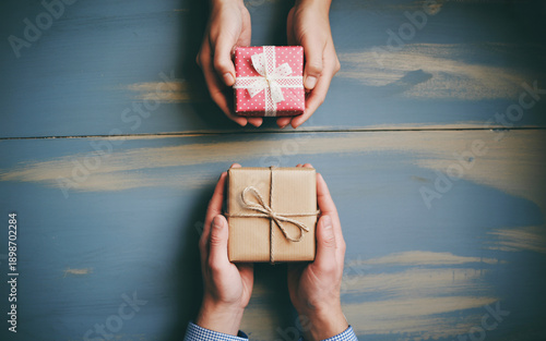 Hands holding small gift box on wooden table, cozy Valentine surprise flat lay