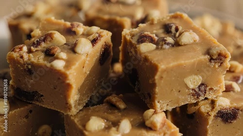 Close-up of homemade fudge squares on a plate, topped with nuts and containing dark fruit