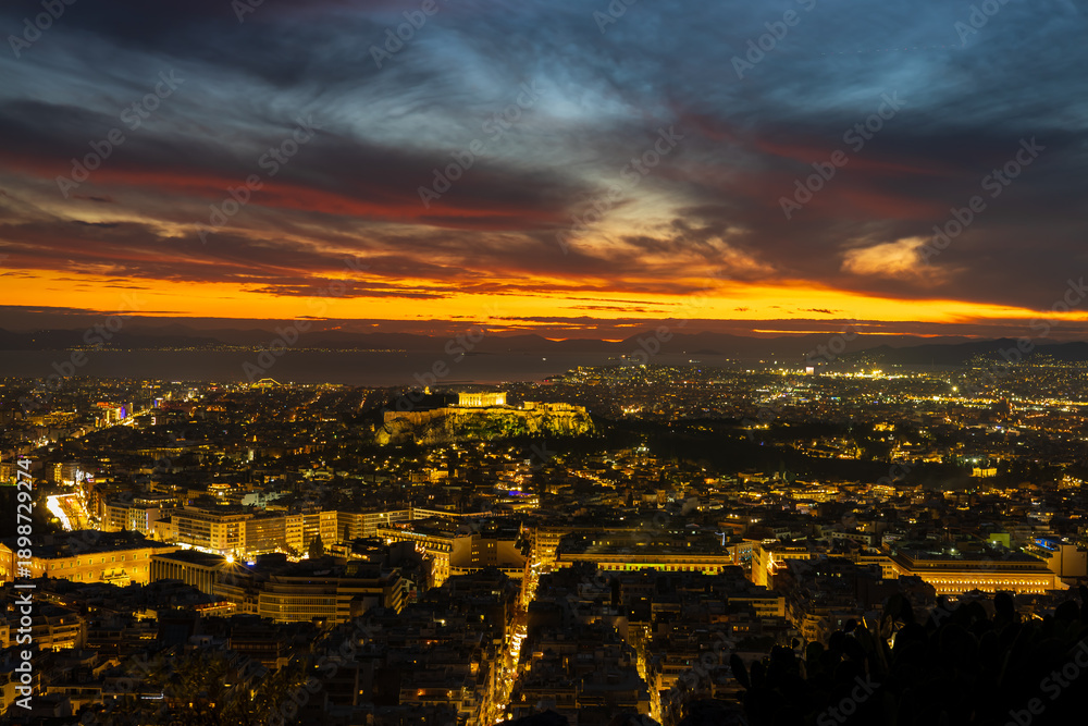 Fototapeta premium Panorama of Athens at sunset with a view of the Acropolis. The city lit up at night against the backdrop of enchanting clouds and a mesmerizing sunset. A peaceful picture of relaxation 