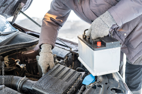 Foto Man replacing car battery in winter cold with open hood during roadside emergenc