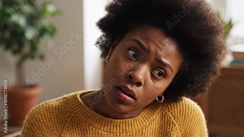 Woman looks uneasy questioning distrustfully expression skeptical inquisitive worried uncertain yellow sweater indoors suspicious doubtful reaction close up