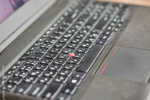 Closeup laptop keyboard with red trackpoint button detail.