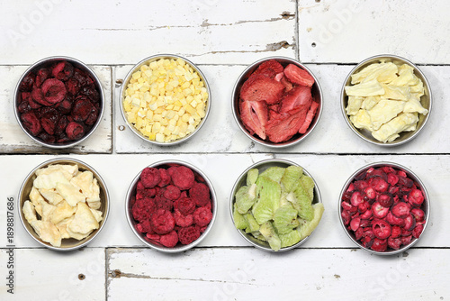 selection of freeze-dried fruits (sour cherries, pineapple, strawberries, kiwi, mango, raspberries, melon, cranberries) in aluminum bowls on rustic wooden background