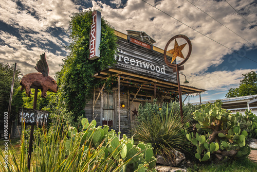Old Rustic Greenwood Saloon Building With Texas and Star Signs Surrounded By Plants in Rural Texas Town