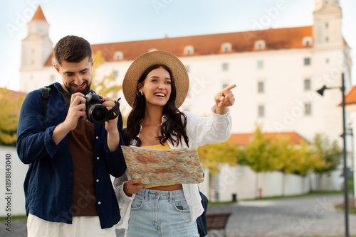 Tourists couple enjoying their time outside walking and looking at landmarks, woman holding map while man taking photos