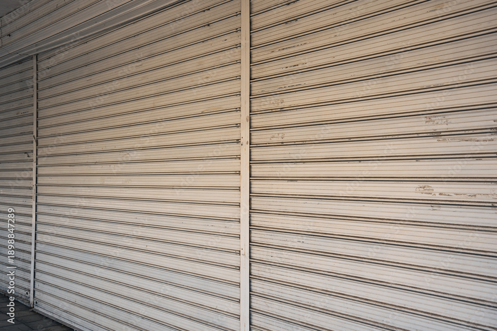 Fototapeta premium Shops in a Bulgarian neighborhood close for the evening and season. Rolling shutters are pulled down, marking the end of the day for local businesses. The street is quiet as day turns to night