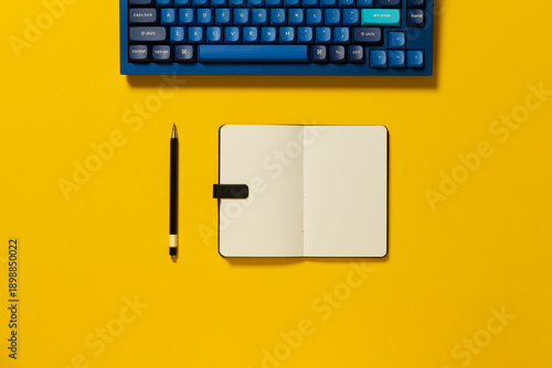 Overhead view of a mechanical keyboard, note pad and pen on colourful background
