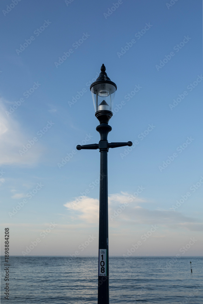 Fototapeta premium Elegant Beachside Lamppost Stands Against Clear Blue Sky by Calm Ocean at Dusk