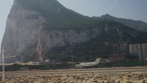 Private airplane departing gibraltar international airport runway with the rock of gibraltar, buildings, and clear sky in the background