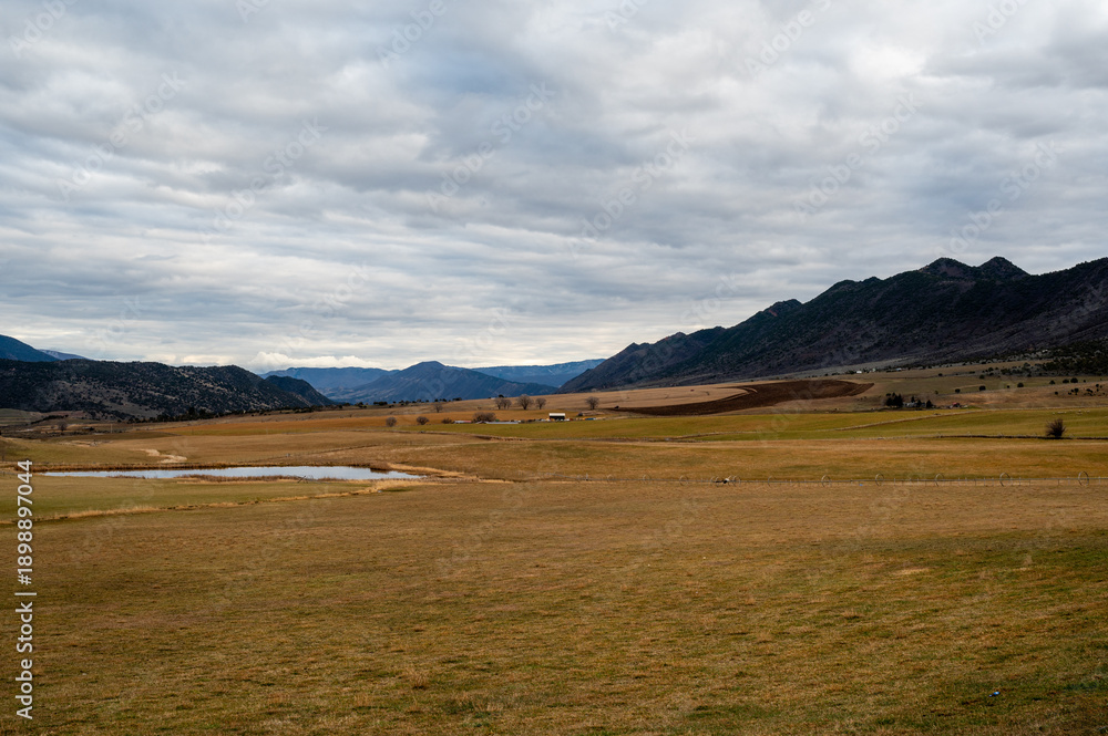 Fototapeta premium Grass Valley sheep farms and pond in Garfield County western Colorado under complex winter cloudscape.