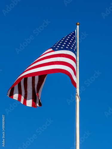 American Flag Flown On Pole Against Clear Blue Sky, Symbol of Freedom and Patriotism Outdoors