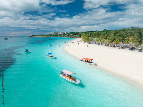 Beautiful tropical beach with turquoise sea and white sand in Kendwa, Zanzibar. Aerial view of coastline with palm trees, clear water, boats, resort. Summer vacation, travel, exotic. Top drone view © den-belitsky