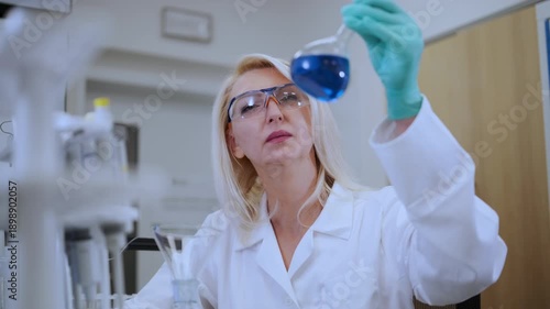 Middle aged female scientist watching chemical solution in glass flask in laboratory. 