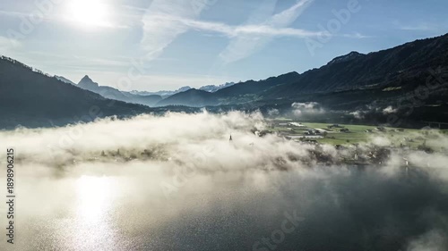 Backlit aerial shot of fogy alpine valley with sun fare and mountains