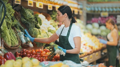 Shop seller put goods on display case. Girl creates stock of bunch of green onion in display case, forms showcase. Vegetable shop near house. Store with long rows of display cases, customers waiting