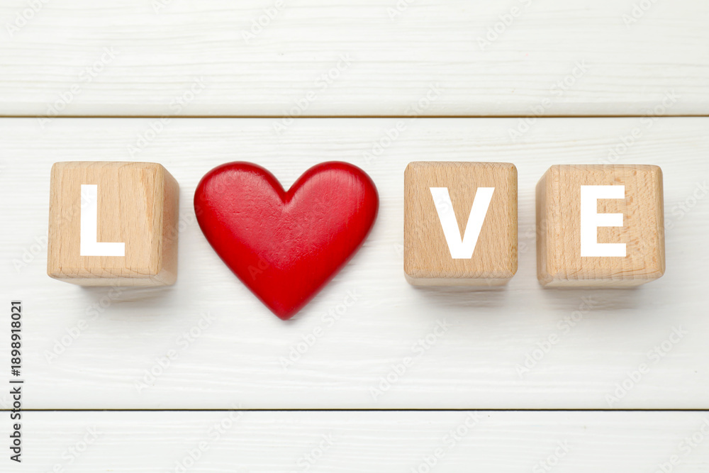 Naklejka premium Word Love made of wooden cubes and red heart on white table, flat lay. Greeting card