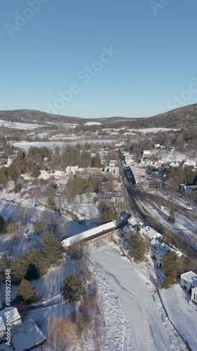 4K Vertical drone aerial video over quaint covered bridge in Woodstock, Vermont village over the Ottauquechee River in winter after recent snowfall and sunshine.