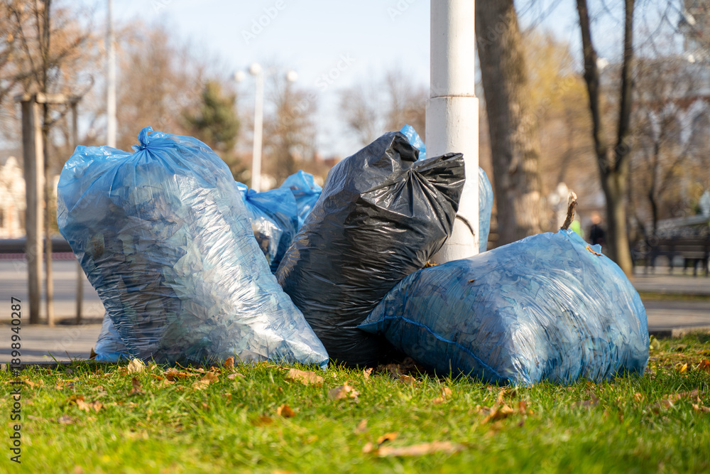 Fototapeta premium Garbage bags piled on grass near street in urban park
