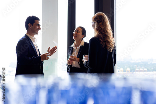 Wallpaper Mural Three business professionals smiling and talking near large office window holding drinks showing friendly networking teamwork confidence and modern corporate culture Torontodigital.ca