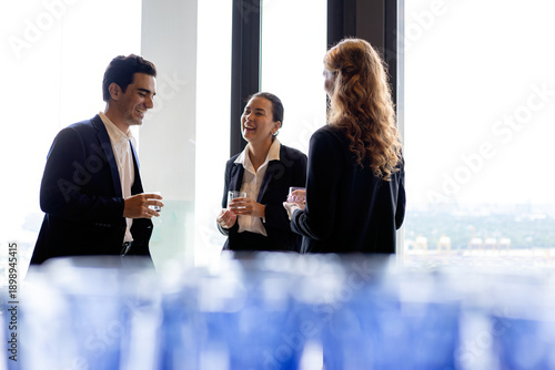 Wallpaper Mural Three business professionals laughing and talking near large office window holding drinks showing friendly networking teamwork confidence and modern corporate culture Torontodigital.ca
