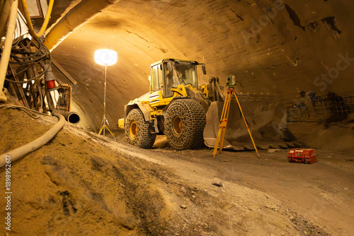 Schilderij op canvas Yellow wheel loader positioned on uneven ground inside a dimly lit tunnel, surve