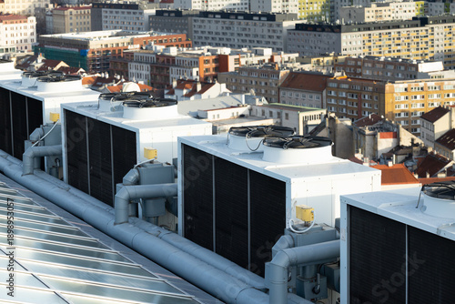Rooftop view of multiple air conditioning units on a building with cityscape background featuring residential and commercial structures in an urban environment