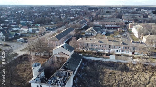 Aerial view captures a quiet village with old residential buildings, bare trees, and a central road. The scene portrays a typical provincial settlement under an overcast sky.
