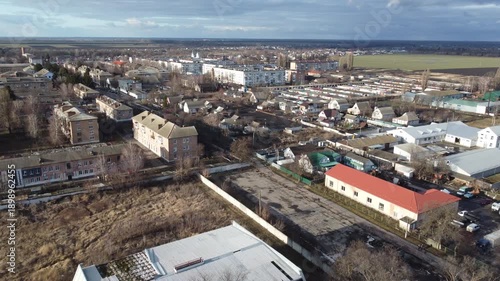 Drone footage captures a suburban residential area with various houses and bare trees under a cloudy sky. The broad perspective offers a glimpse into the everyday life of a small town community.