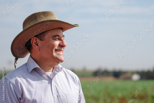 Fotografie Portrait of a smiling middle-aged farmer wearing a straw hat in a green agricult