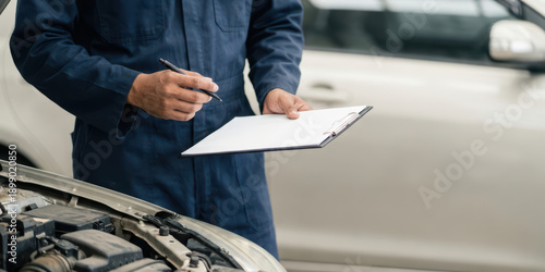 Auto car check up job with mechanic writing clipboard repair at work garage banner scene shows professional worker near vehicle during routine service inspection in bright clean workshop