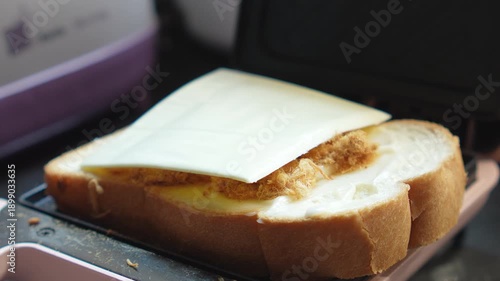 Wallpaper Mural 4K Close-up person placing a slice of white cheese on bread with dried shredded pork in a sandwich maker, Homemade breakfast prep cooking simple meals. Torontodigital.ca