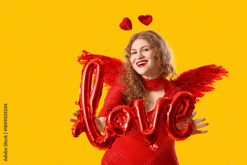 Fototapeta premium Beautiful woman dressed as Cupid with word LOVE made of balloons on yellow background. Valentine's Day celebration