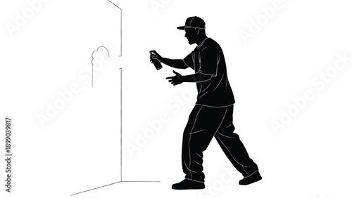 Silhouette of a young man wearing a backwards baseball cap creating street art with aerosol paint on a white corner surface