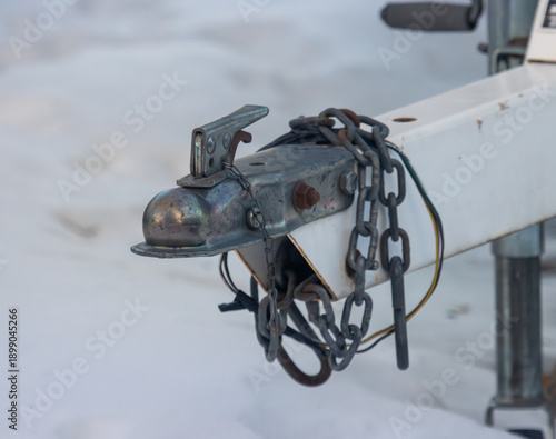 A hitch coupler with safety chains and electrical plug on a trailer parked in the snow