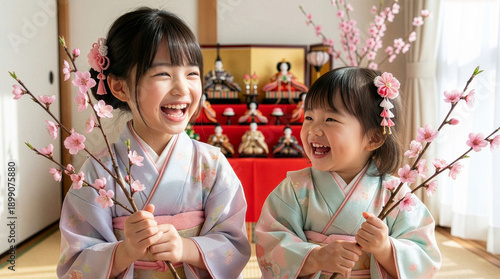 ひな祭りで桃の花が咲く枝を持つ笑顔の姉妹