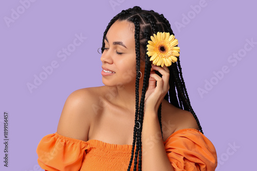 Beautiful young African-American woman with gerbera flower on purple background