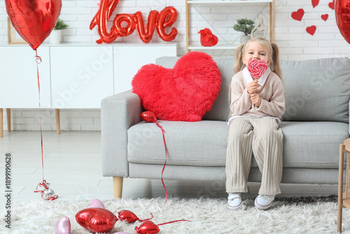Cute little girl with lollipop sitting in room decorated for Valentines Day