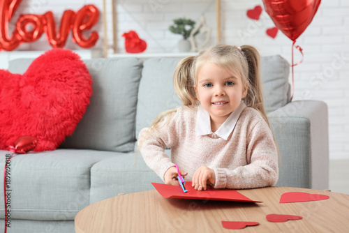 Cute little girl cutting paper hearts in room decorated for Valentines Day
