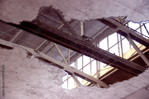 A puddle of fuel and water on a concrete floor with reflections of the ceiling and window structures inside the building