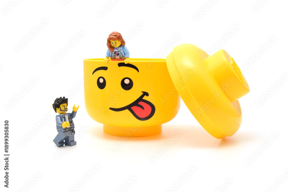 Fototapeta premium Lego minifigures are at the large yellow head with funny face is sticking out the tongue isolated on white. Editorial illustrative image of popular plastic toy.