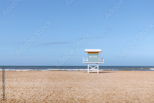 Spring Deauville beach with lifeguard station shows complete solitude, solitude extending across empty sand and calm water, solitude creating reflective and serene coastal mood