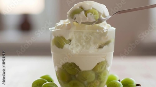A spoon lifting a serving of gooseberry fool dessert from a glass, ready to eat, displayed on a table indoors.