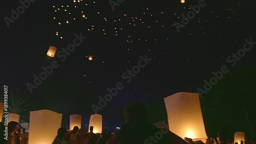 Beautiful floating lanterns rising into the dark night sky during Yee Peng Festival in Thailand. People releasing traditional paper lamps for luck and celebration.