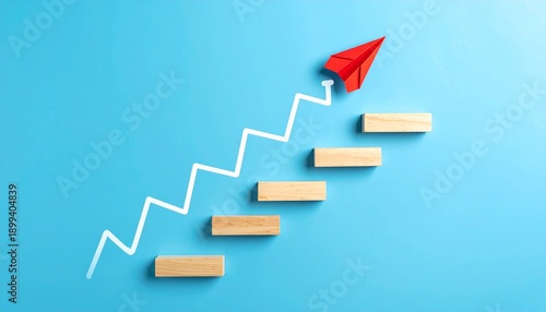 Conceptual image representing progress and aspiration, featuring a white zigzag staircase line on a blue background with five wooden rectangular blocks placed at each step; a red paper airplane positi