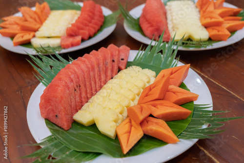 Plates of neatly arranged tropical fruit slices served on banana leaves.