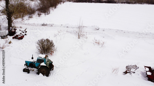 Obraz na plátně Aerial View of a Weathered Blue Tractor in a Snowy Village Yard