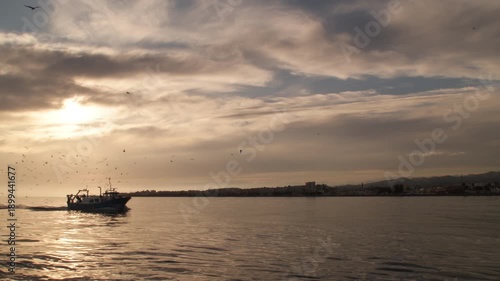 Fisher ship entering to port at sunset