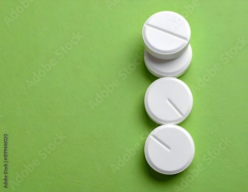 White circular tablets with score lines stacked on a green background