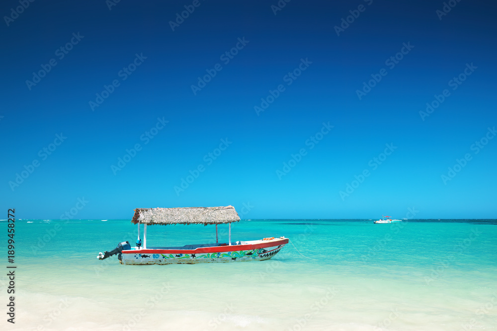 Obraz premium Traditional wooden boat with thatched roof floating on crystal clear turquoise waters of Caribbean sea, near Punta Cana, Dominican republic