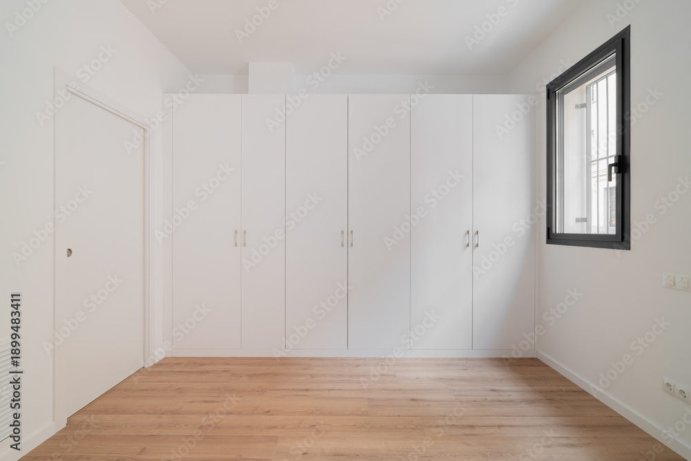 custom made wallpaper toronto digitalA minimalist interior of a room with white walls and a wooden floor. A large white wardrobe occupies one wall. A window allows natural light to enter.